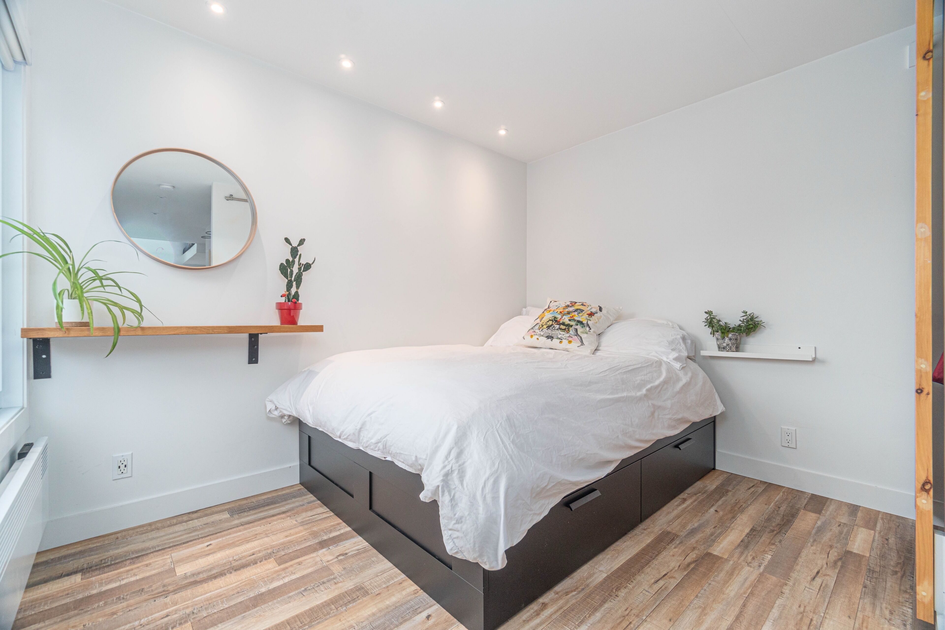 Un dormitorio moderno con una cama, un espejo redondo y dos estantes con plantas.