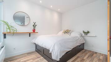 Un dormitorio moderno con una cama, un espejo redondo y dos estantes con plantas.