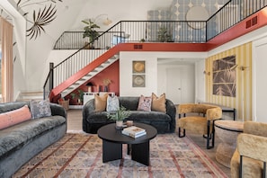 Un vaste espace de vie agrémenté d’une table basse noire, de canapés gris et d’un escalier aux touches de rouge.
