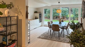 A modern kitchen with white cabinets, a dining area with a table and chairs, and a large window overlooking a garden. - Beautiful home in Dronningmølle with WiFi (Dronningmølle)