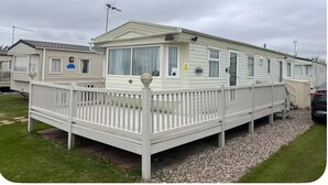 Une maison mobile dotée d’une terrasse clôturée, d’une antenne parabolique et d’un panneau indiquant que les animaux de compagnie sont les bienvenus.