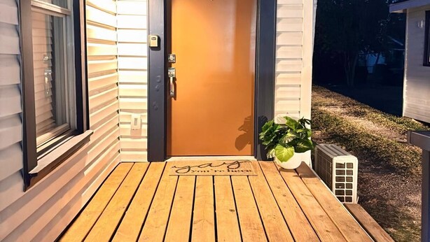 Un portico in legno con una porta, una pianta in vaso e un tappetino d'ingresso.