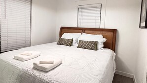 Un letto rifatto con un patchwork bianco e due cuscini, una testiera in legno e un lampadario a soffitto.