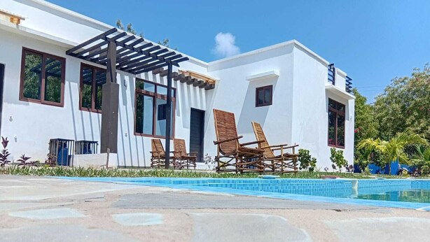 Ein modernes, weißes Gebäude mit Pool, Holzliegen und einer Pergola.