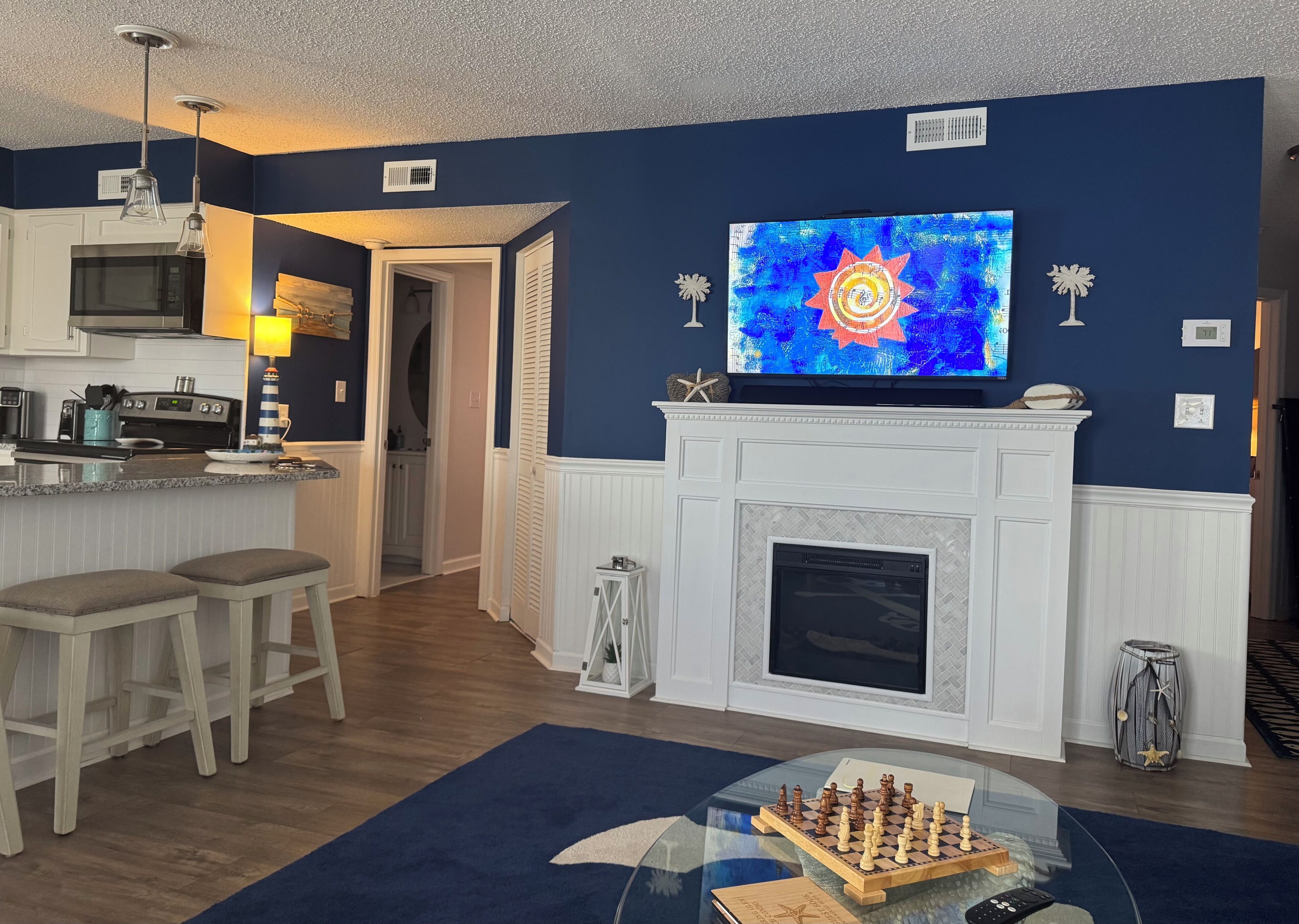 Una sala de estar con chimenea, televisor y un tablero de ajedrez sobre una mesa de vidrio.
