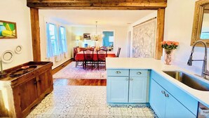 A dining area with a wooden ceiling, a kitchen with blue cabinets, and a tiled floor.