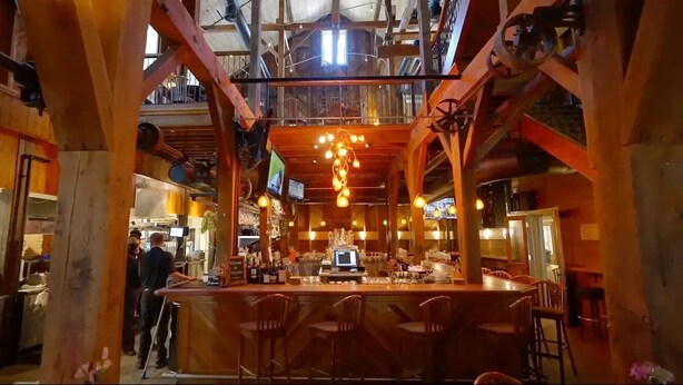 A bar area with wooden beams, hanging light fixtures, and a bar counter with stools.