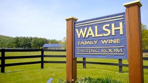 A sign for Walsh Family Wine Tasting Room with a wooden fence and greenery in the background.