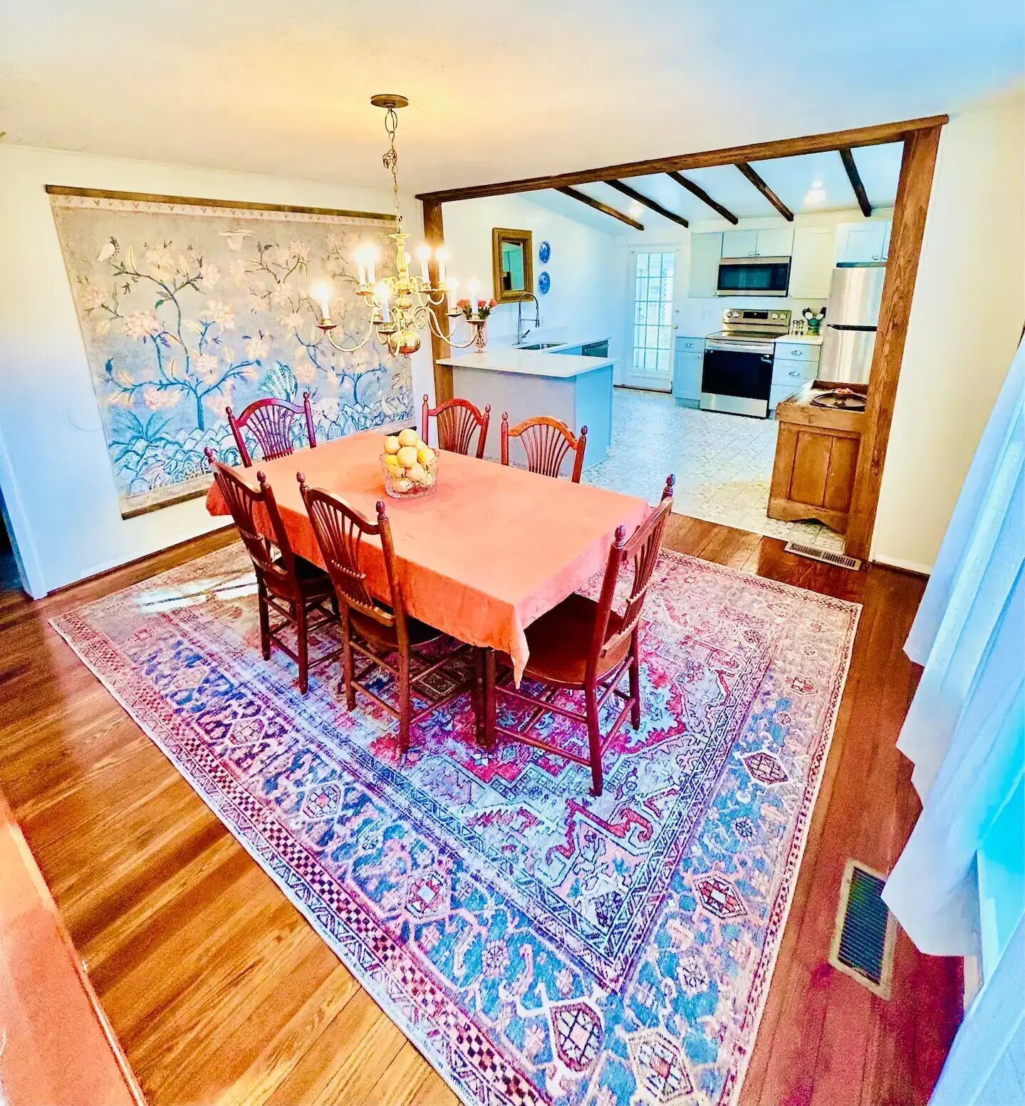 Zona pranzo con tavolo e sedie in legno, tappeto decorato e lampadario.