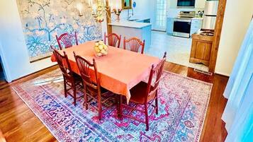 Zona pranzo con tavolo e sedie in legno, tappeto decorato e lampadario.