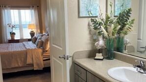 A hotel room with a bed, a bathroom with a sink, and a window with curtains. - Coastal Comfort retreat offers 1 Bedroom, 1 Bathroom, and a Futon with Lakeview. (Jacksonville)