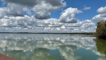 A calm lake with a wooden dock extending into the water, surrounded by trees and a cloudy sky.