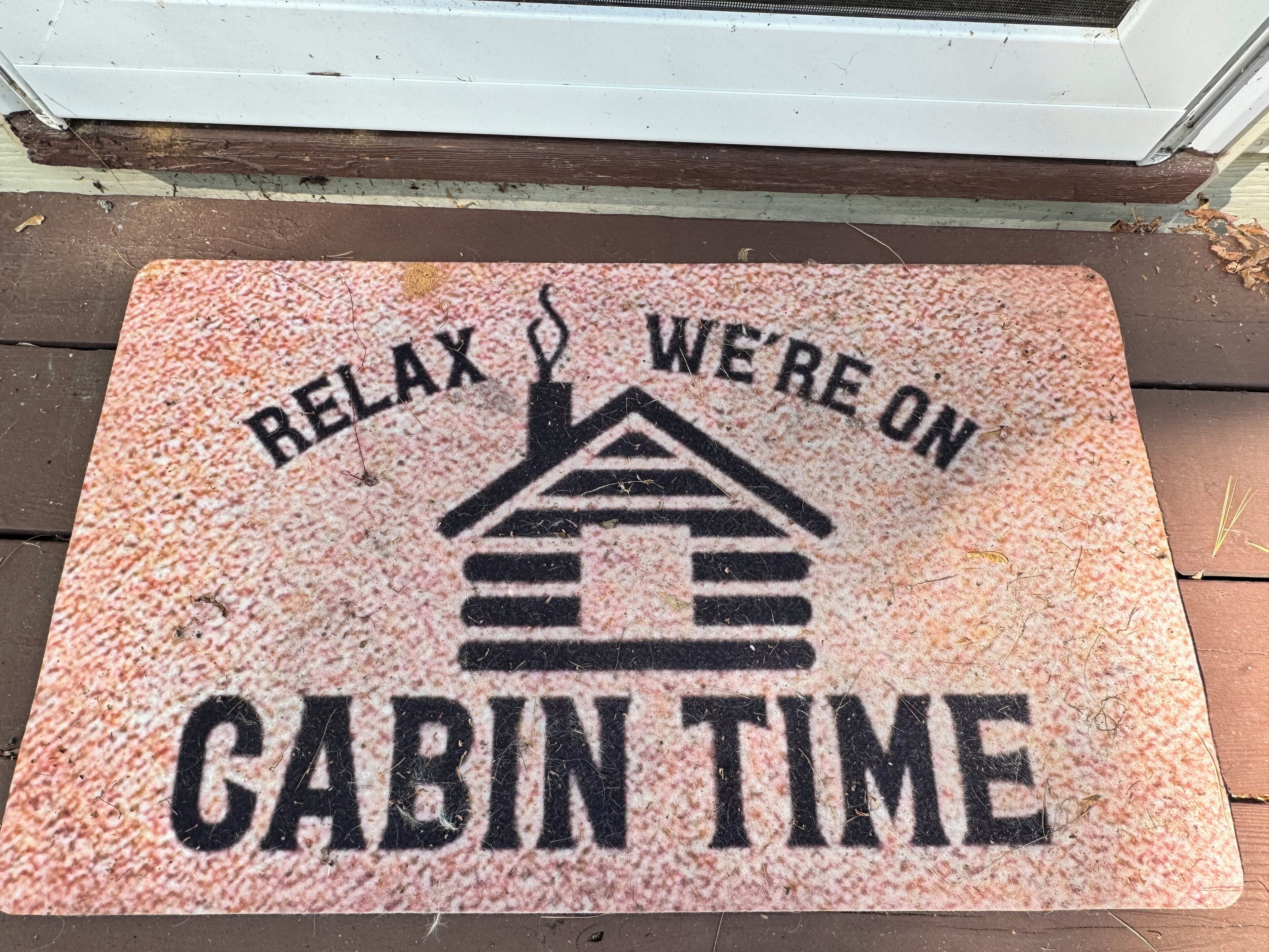 Alfombra de entrada con el texto "RELAX WE'RE ON CABIN TIME" y un icono de casa.