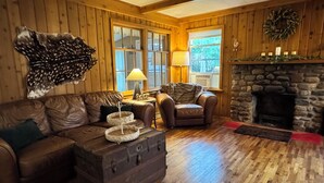 Ein gemütliches Blockhauss-Interieur mit Holzboden, Ledermöbeln, einem Steinkamin und einem Fellteppich.