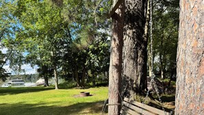 Ein Park mit einer hölzernen Bank unter einem Baum, einer Rasenfläche und einem See im Hintergrund.