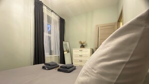 Una cama bien hecha con toallas dobladas, un espejo en la mesita de noche, un aparador y una puerta.