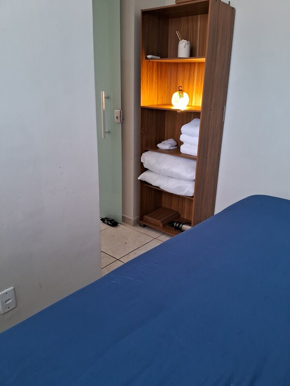 A room with a bed, a wardrobe with shelves, and a small table with a lamp.