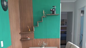Een eetgedeelte met een glazen tafel, twee beige stoelen, een vaas met gedroogde bloemen en een houten trap tegen een groene muur.