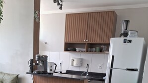 Een moderne keuken met een witte koelkast, een koffieapparaat en een magnetron. Er staat een eettafel met stoelen en een potplant.