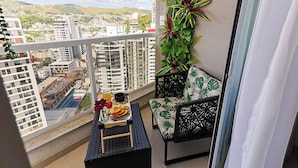 A balcony with a view of a cityscape, a small table with a tray of food, a chair, and a plant wall. - Studio Pet Friendly c Garagem e Varanda no Centro (Juiz de Fora)