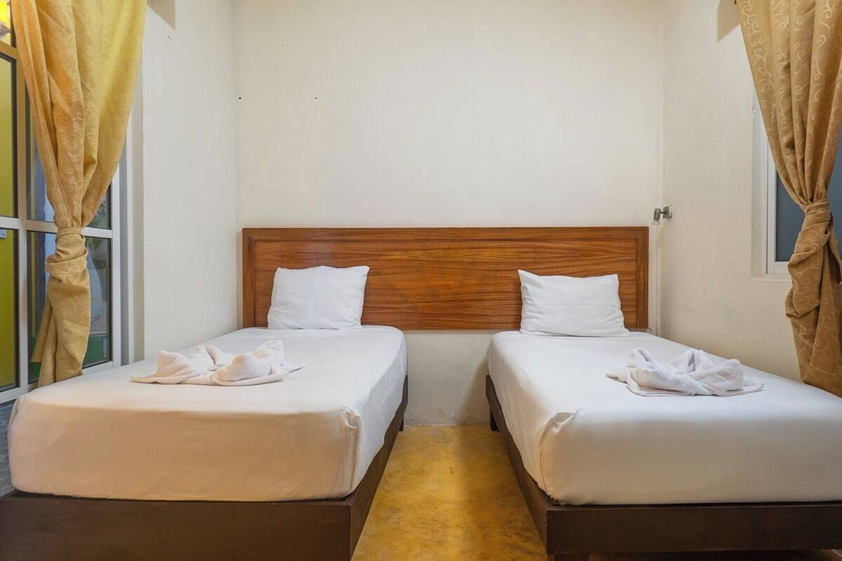A room with two single beds, wooden headboards, white bedding, and a window with curtains.