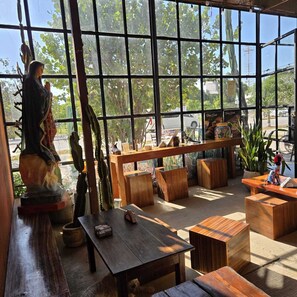 A cozy cafe with large windows, wooden furniture, and a statue. - Casa Frida (Tulum)