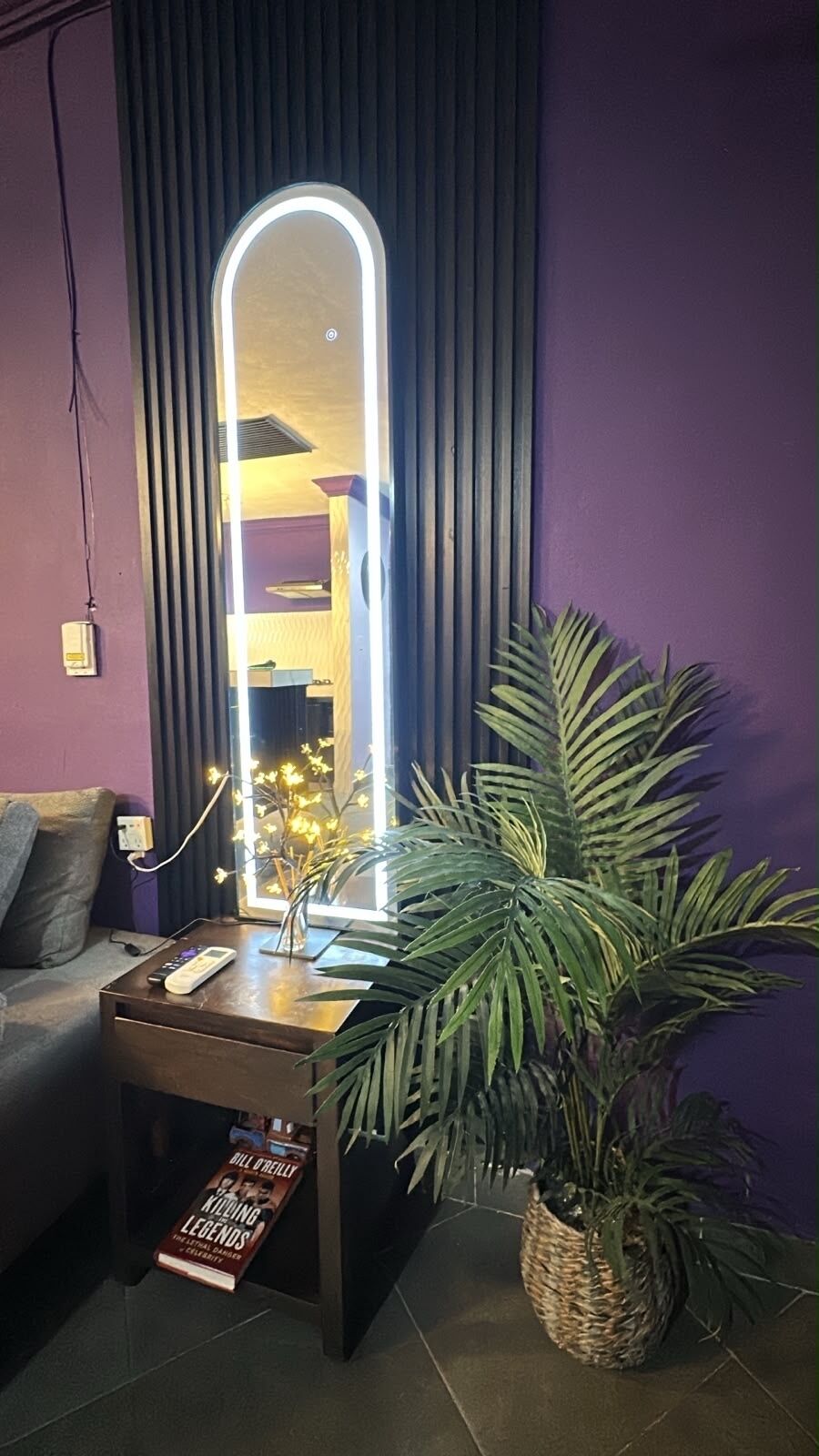 Une pièce avec un mur violet, un grand miroir, une petite table avec une plante et un canapé.