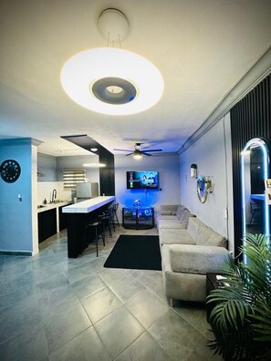 Una sala de estar moderna con un sofá, un televisor y una zona de cocina con una mesa de comedor.