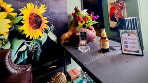 Skilt fra en kaffebar, et fjernsyn, en sofa, en vase med blomster og en flaske på et bord.