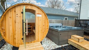 A wooden sauna with a glass door, a hot tub, and wooden steps leading to the sauna. - Brand New HGTV-Quality Family Retreat: Hot Tub, Sauna & Arcades (Indianapolis)