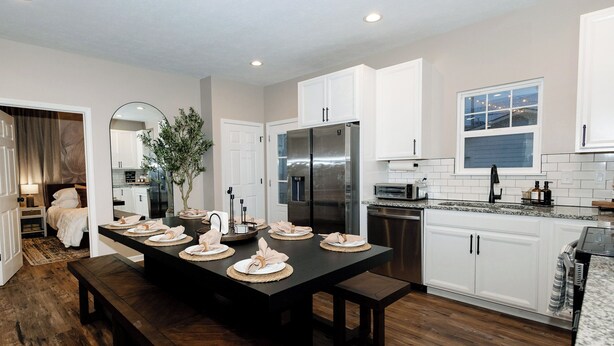 A modern kitchen with white cabinets, a stainless steel refrigerator, and a dining area with a dark wooden table set for four. - Brand New HGTV-Quality Family Retreat: Hot Tub, Sauna & Arcades (Indianapolis)