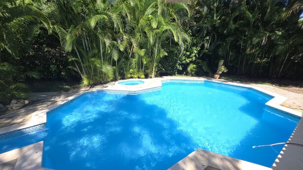 A rectangular swimming pool with a tiled edge, surrounded by lush greenery and a stone deck. - 3-bedroom villa in beautiful Sosúa with cool AC breeze (Sosúa)