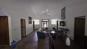 A spacious living area with a high ceiling, a ceiling fan, a large window, and a television on a stand. - 3-bedroom villa in beautiful Sosúa with cool AC breeze (Sosúa)