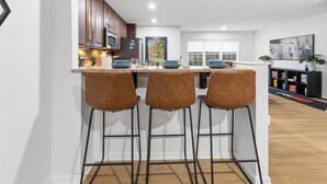 A modern kitchen with wooden cabinets, a central island with bar stools, and a view of the outdoors through a window. - Amazing remodeled property in the Heart of Indy (Indianapolis)