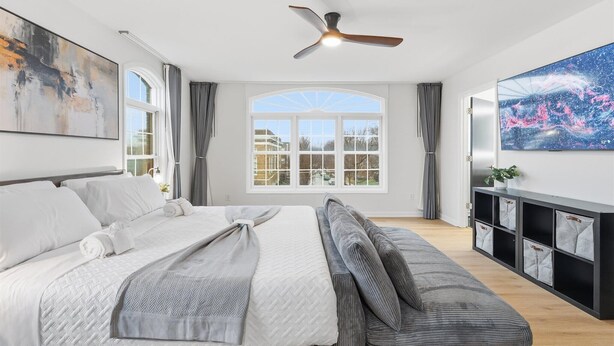 A modern bedroom with a bed, a sofa, a ceiling fan, a large window, and a wall-mounted TV. - Amazing remodeled property in the Heart of Indy (Indianapolis)