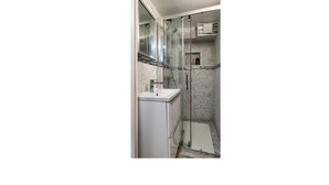 Une salle de bain moderne avec une douche à l’italienne en verre, un lavabo blanc et un mur recouvert de carreaux.