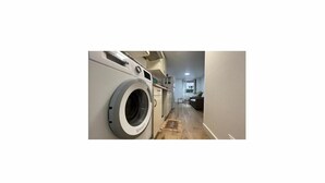 Une buanderie équipée d’un lave-linge à chargement frontal, d’une petite fenêtre et d’un plancher en bois.