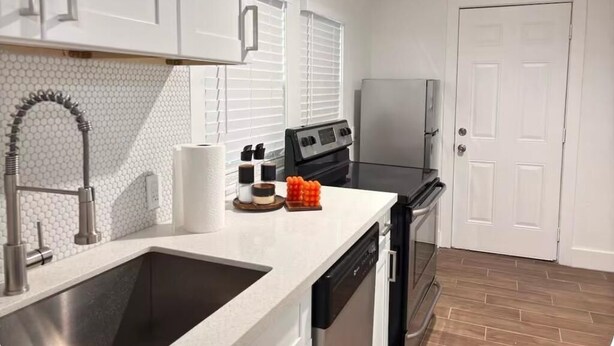 A kitchen with white cabinets, a stainless steel sink, a black stove, and a white refrigerator. - Relax in this cozy home near downtown & stadiums with everything you need. (Houston)