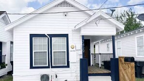 A white mobile home with a blue door, a porch, and a small deck. - Relax in this cozy home near downtown & stadiums with everything you need. (Houston)