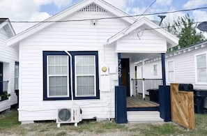 A white mobile home with a blue door, a porch, and a small deck. - Relax in this cozy home near downtown & stadiums with everything you need. (Houston)