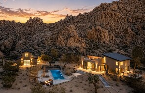 A modern house with a pool, surrounded by desert vegetation and rocky mountains.