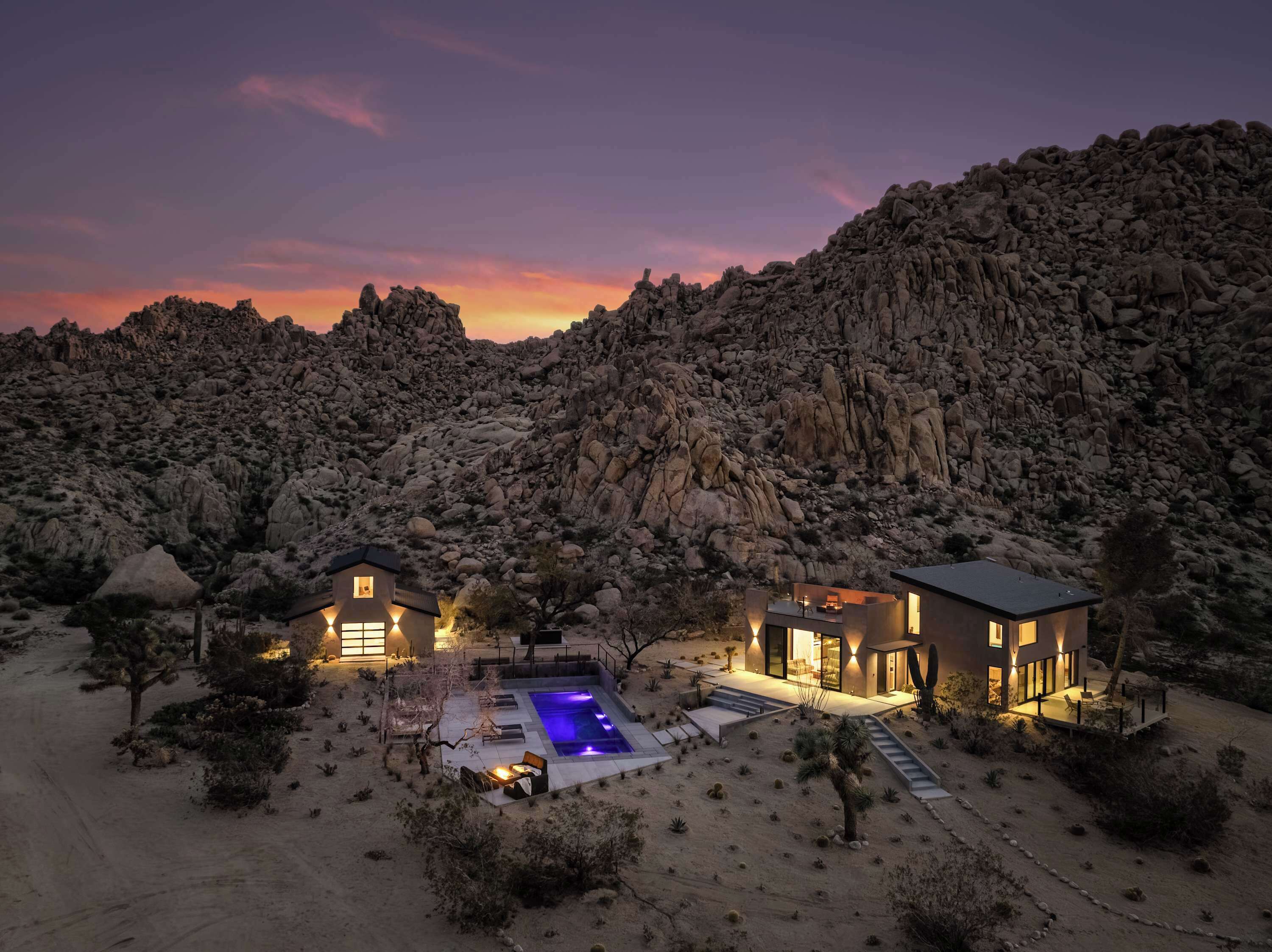 Un resort en el desierto con piscina, dos casas de huéspedes y montañas al fondo.