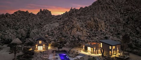 Un resort en el desierto con piscina, dos casas de huéspedes y montañas al fondo.