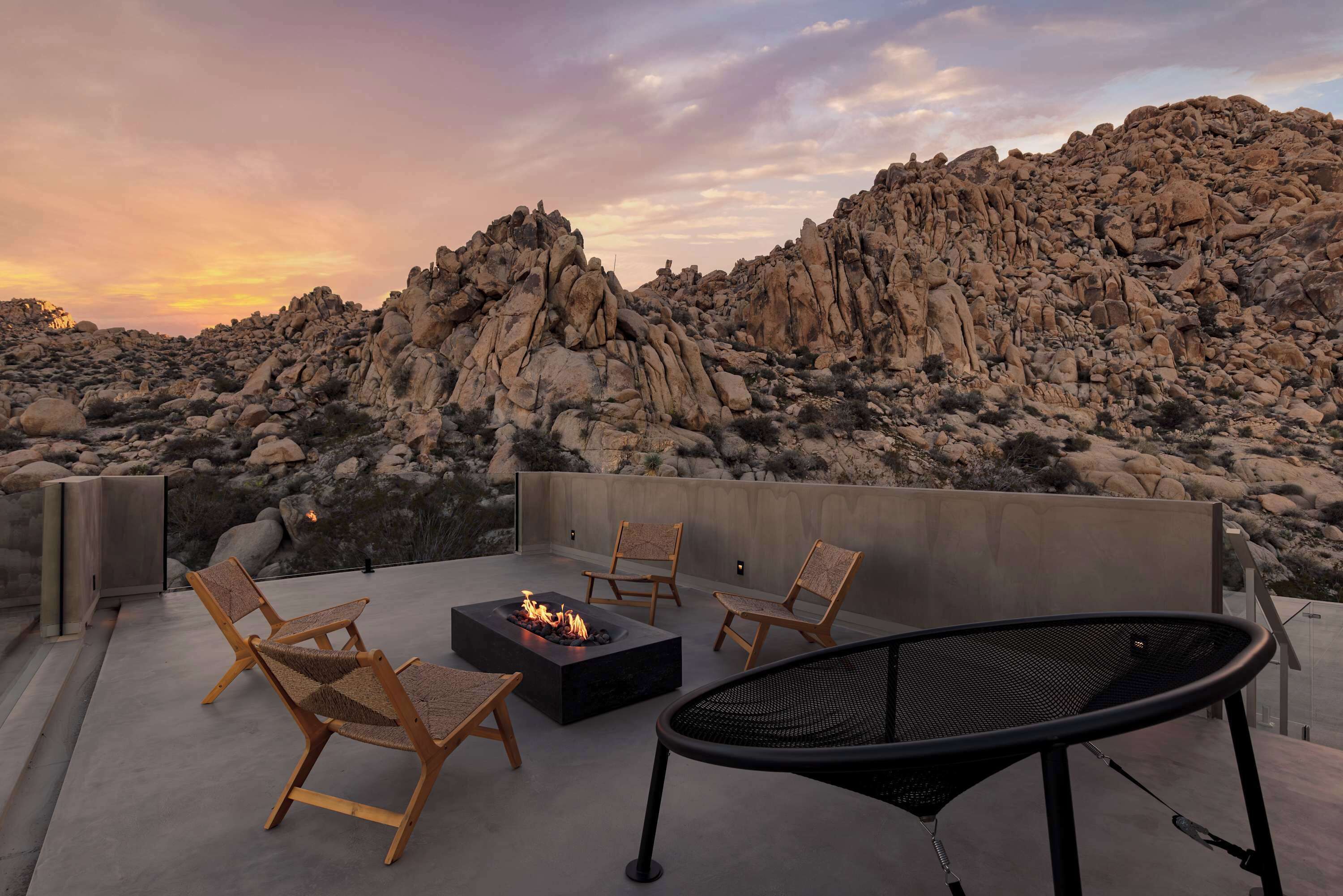 A rooftop terrace with a fire pit, seating, and a view of rocky terrain.