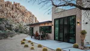 Un bâtiment moderne doté de grandes fenêtres, un patio agrémenté de cactus ronds et un paysage désertique.