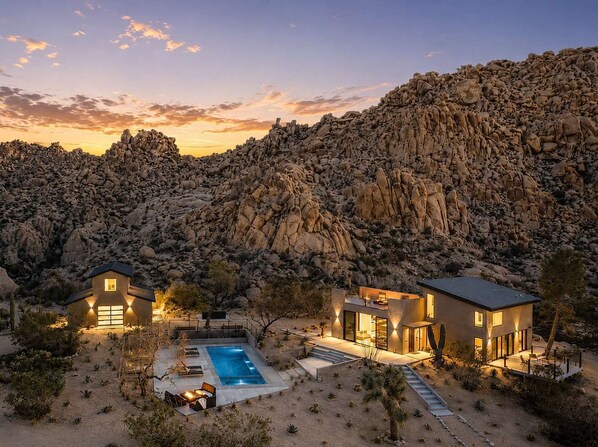 A desert landscape with a pool, two modern houses, and a rocky mountain backdrop.