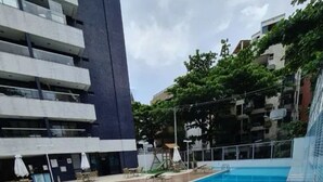 Una piscina con muelle de madera, sillas de descanso y un edificio con varios balcones al fondo.