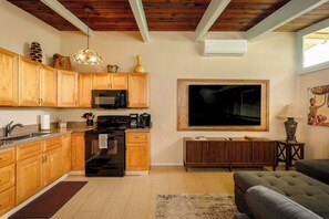 A kitchen with wooden cabinets, a black stove, and a microwave. There's a dining area with a couch and a TV mounted on the wall.