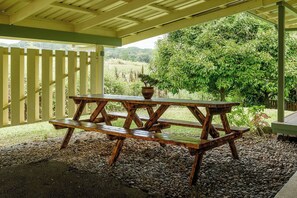 A wooden picnic table with a potted plant on it, set on a gravel surface under a wooden pergola.