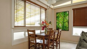Een eetruimte met een houten tafel en stoelen, een vaas met bloemen en een schilderij aan de muur.